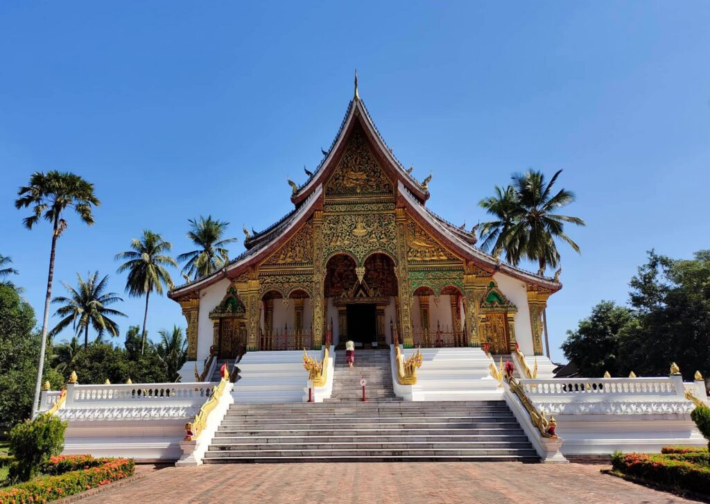 Templo Wat Xieng Thong em Laos, uma construção com traços ocidentais em tons de ouro, verde e vermelho, com uma escadaria branca que leva a entrada do local, para representar o seguro viagem para Laos