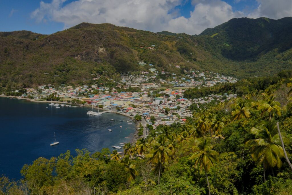 Castries, uma orla com alguns barcos parados, após a faixa de areia é possível ver uma pequena cidade que está localizada entre duas montanhas, o mar é azul escuro, para representar o seguro viagem para Santa Lucia
