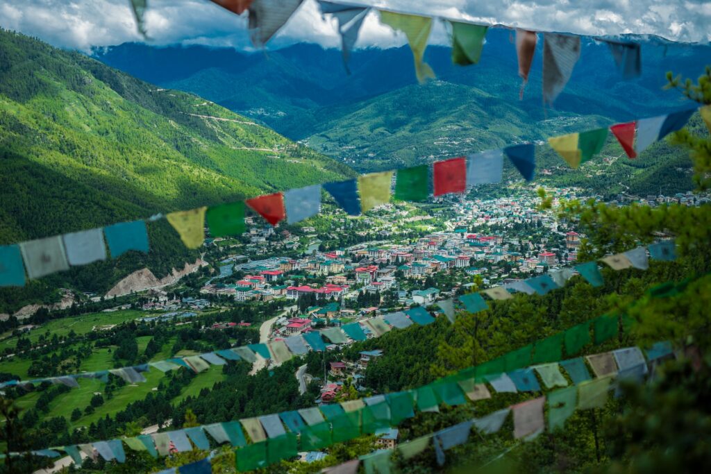 Thimpu, a capital de Butão, uma cidade com telhados coloridos entre as montanhas verdes e com algumas bandeiras coloridas presas na vegetação das montanhas, para representar o seguro viagem para Butão