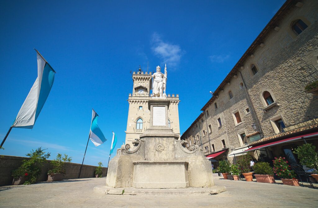 Praça della Libertà em San Marino, um local com construções em estilo medieval, uma monumento central de um homem segurando uma bandeira enrolada, para representar o seguro viagem para San Marino