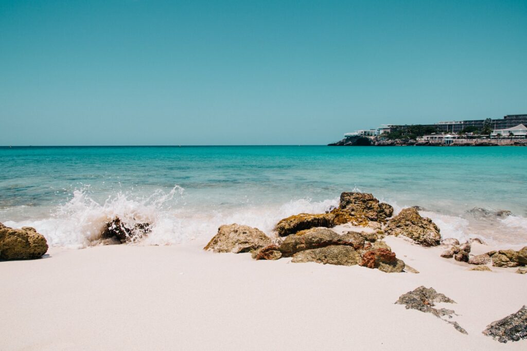 Praia Maho em St Maarten, areia branca, mar de águas claras, com algumas rochas na areia