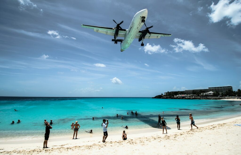 Praia Maho em St Maarten, um avião sobrevoa muito baixo a praia, os turistas ficam parados na areia avistando o avião e tirando fotos, o mar é azul claro 