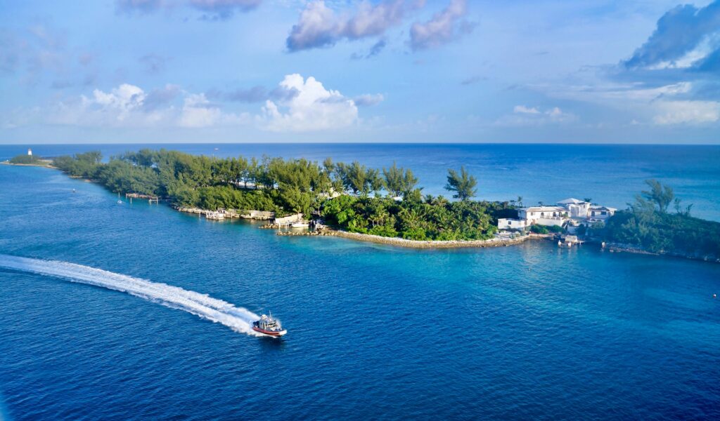 Nassau nas Bahamas, uma ilhota pequena com muita vegetação e algumas construções, o mar escuro ao redor, uma pequena embarcação passa pelo mar, para representar o seguro viagem para Bahamas