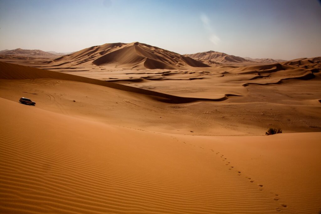 Deserto Rub Al Khali em Omã, um amplo deserto laranja, com montanhas e um carro passando pelo local, para representar o seguro viagem para Omã