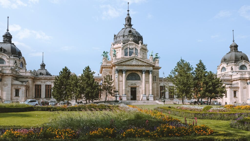 Vista da faixada do Termas de Széchenyi, com jardim a frente. Representa o seguro viagem para Budapeste.