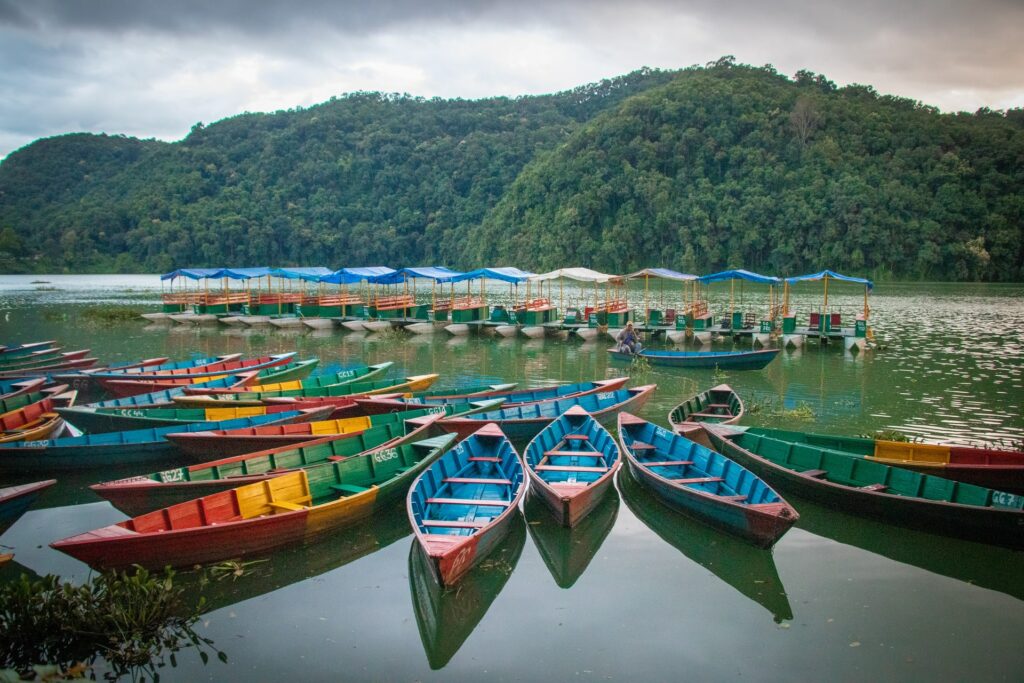 Distrito de Pokhara no Nepal, um enorme lago com barquinhos coloridos flutuando e, ao fundo, muitas montanhas cobertas por vegetação, para representar o seguro viagem para o Nepal