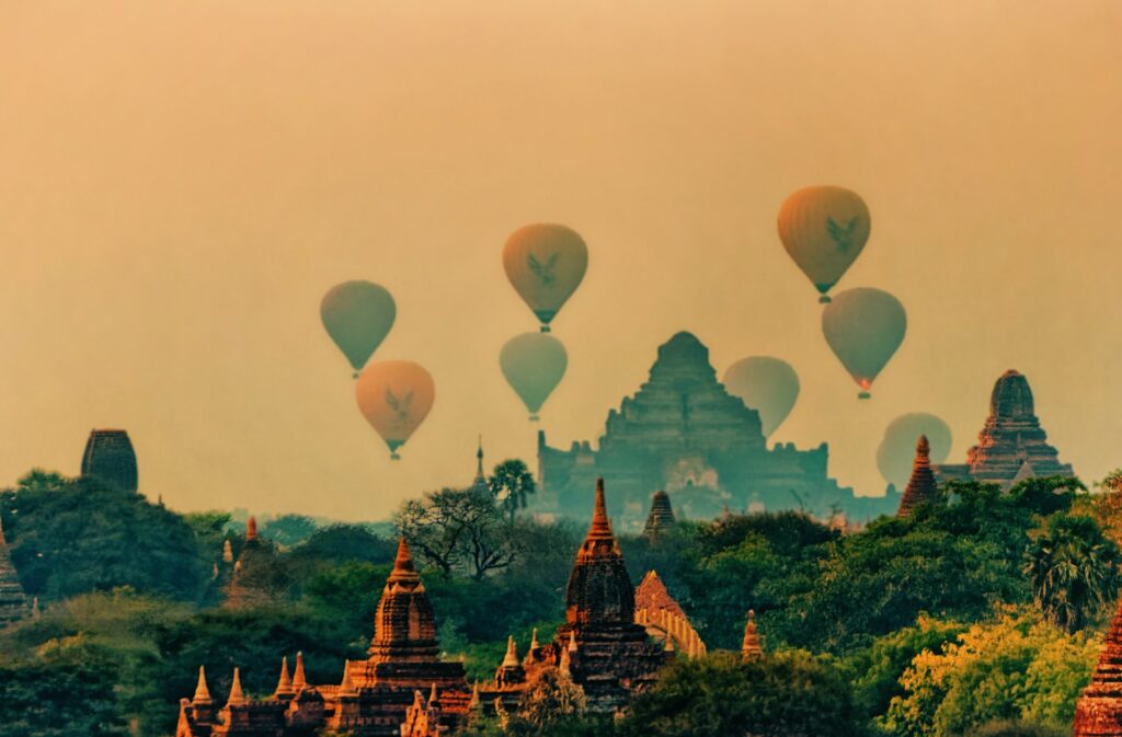 Cidade de Bagan em Mianmar, um local com diversos balões de ar flutuando, muitas montanhas, vegetação rica e o topo de templos sendo cobertos pela neblina, para representar o seguro viagem para Mianmar