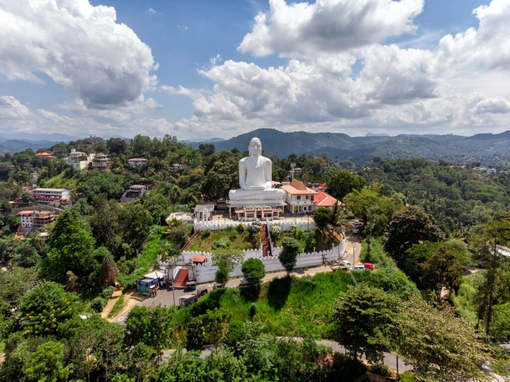 Uma estátua branca de buda sob um templo, cercado por vegetação, algumas outras casas, para representar o seguro viagem para o Sri Lanka
