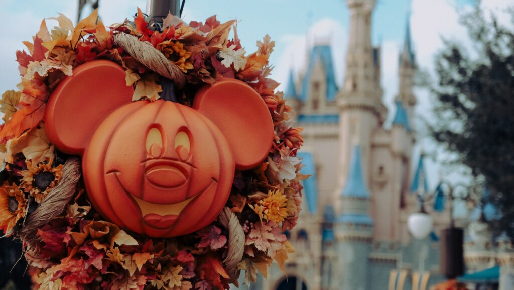 vista do Magic Kingdom com o castelo da Cinderela ao fundo desfocado e, na frente, uma cabeça de Mickey esculpida de uma abóbora com folhas alaranjadas, na Disney