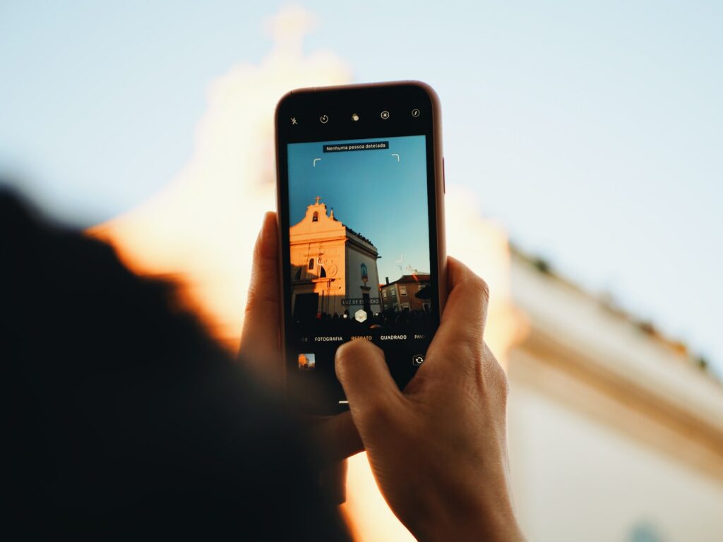 Um celular na vertical sendo segurado por mãos brancas para fotografar um prédio antigo em uma rua de Aveiro em Portugal