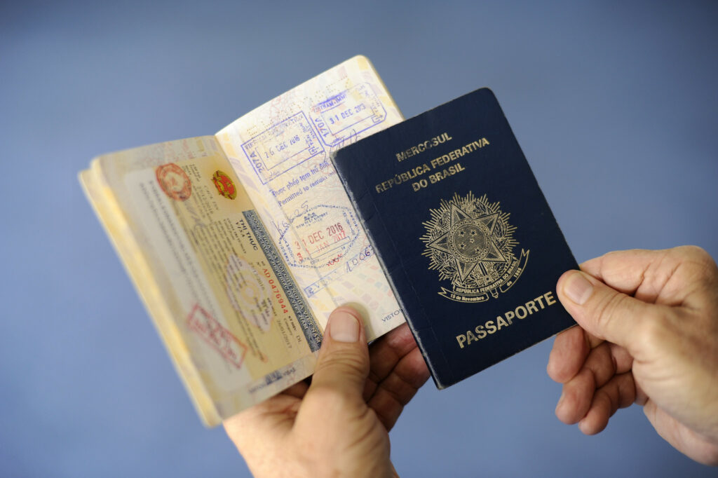 Uma mão masculina segurando um passaporte brasileiro