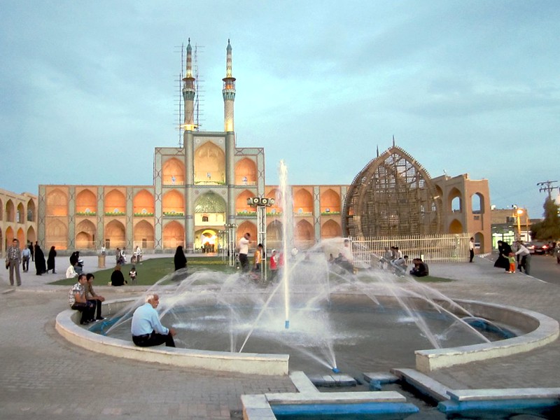 Pessoas sentadas ao redor de uma fonte de água e espalhadas pelo Amir Chakhmaq Complex no Irã durante o dia.