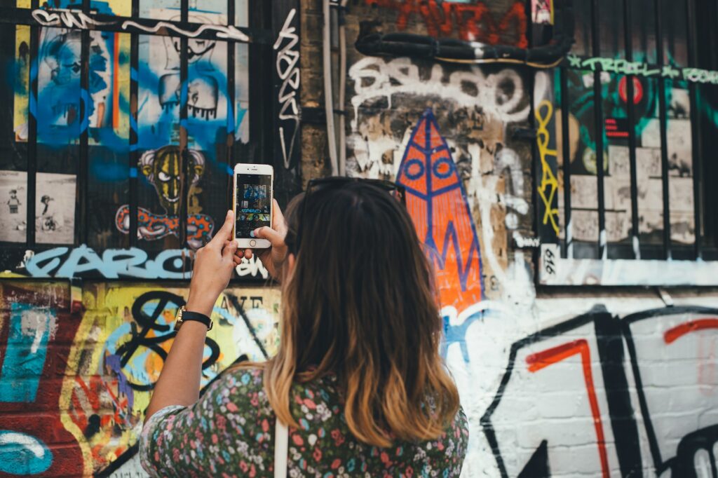 Uma mulher segurando um celular na vertical fotografando um muro cheio de pichações e desenhos, para representar o chip internacional para Londres