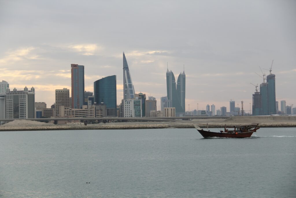 Vista do mar de Manama, Bahrain, durante o dia com barco no mar e ao fundo a cidade com prédios. Representa seguro viagem para Bahrein.