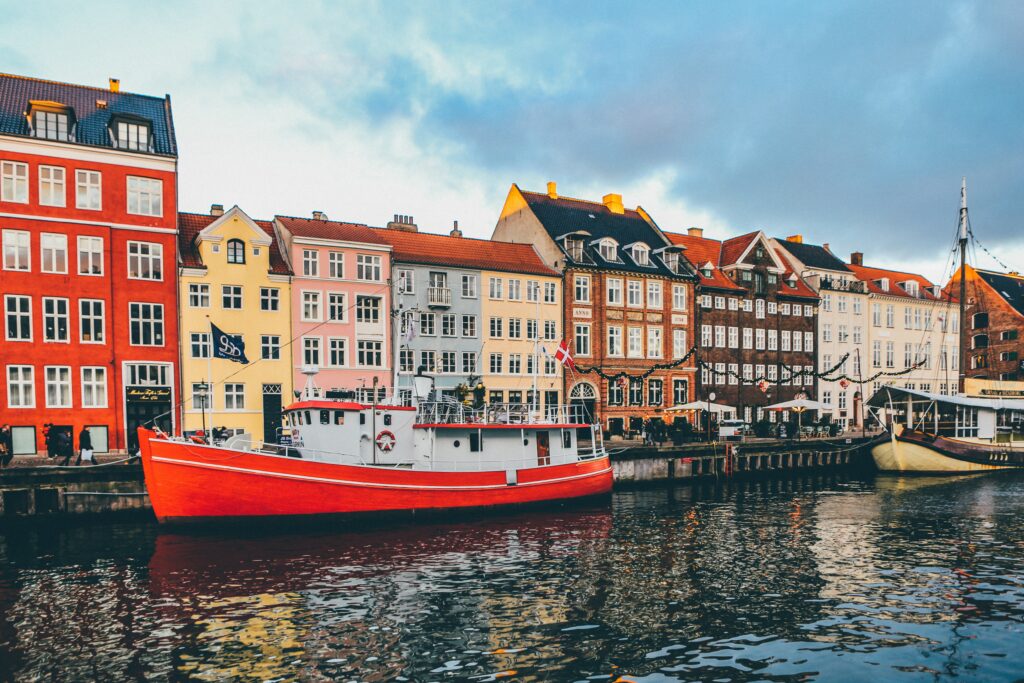 Barco de cor vermelha e branco no rio e ao fundo prédios coloridos durante o dia em Nyhavn. Representa chip internacional para a Dinamarca.