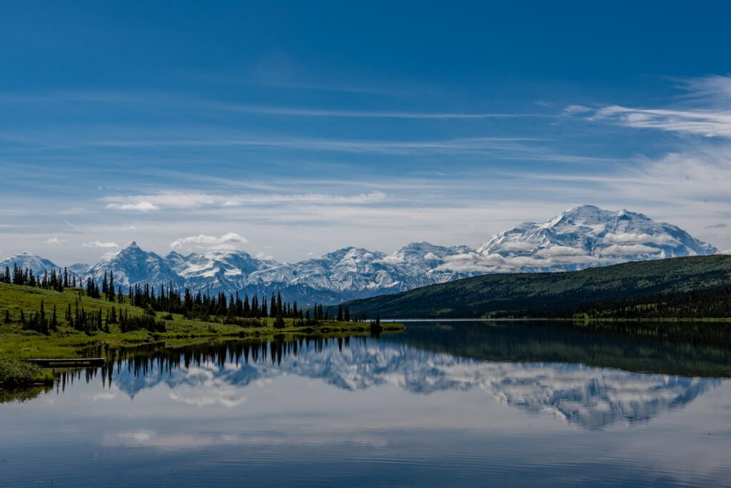 Um amplo lago com montanhas nevadas ao fundo, e um campo com algumas árvores, para representar chip internacional para o Alasca