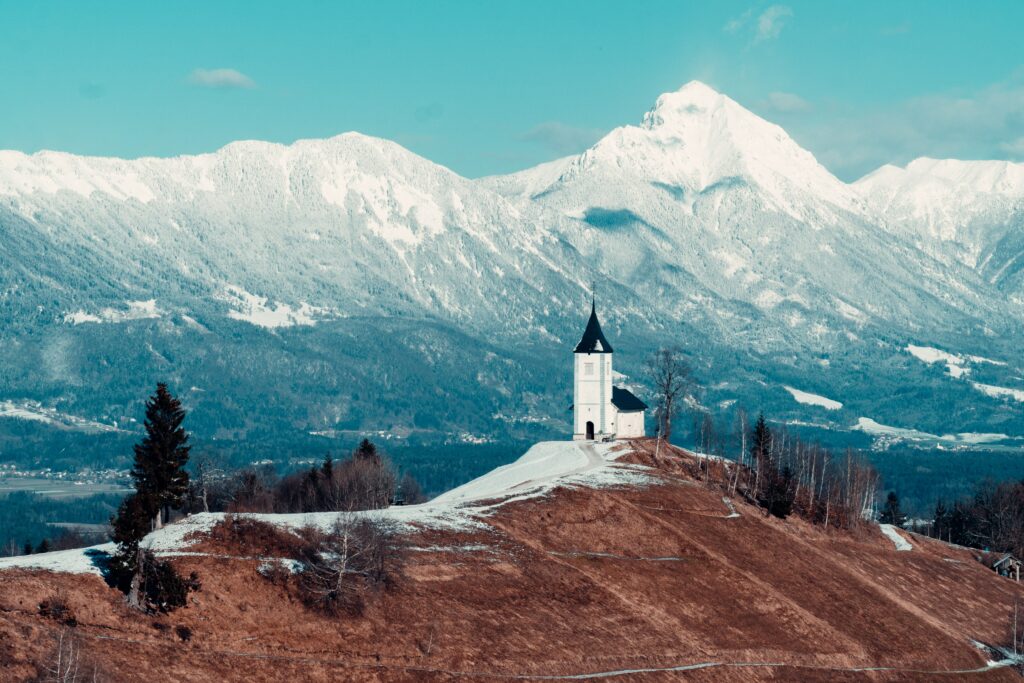 No meio da montanha a  Igreja de St. Primož perto de Jamnik na Eslovênia durante o dia em volta das montanhas.