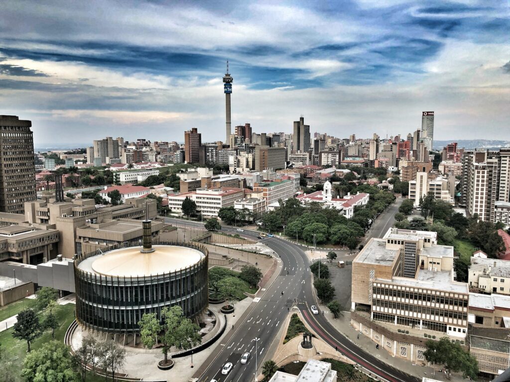 Fotografia aérea do centro urbano de Johanesburgo durante o dia. Com casas, prédios e vias onde passam carros e pedestres. 