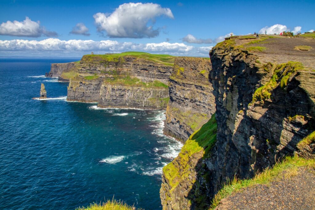 Montanha rochosa em tons de cinza e verde ao lado do mar azul durante o dia, ilustrando post chip internacional para a Irlanda.