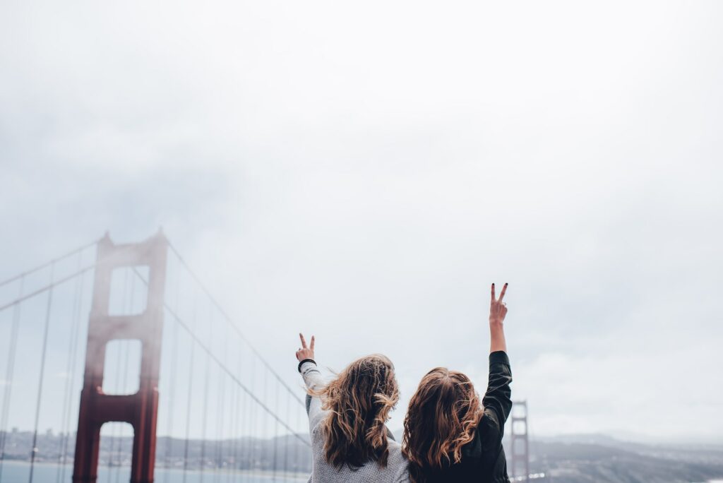 duas garotas de costas fazendo sinal da paz com a Ponte Golden Gate em San Francisco, um dos locais que recebem visitantes que utilizam o seguro viagem para intercâmbio
