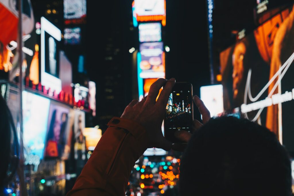 Uma pessoa segurando um celular na vertical tirando fotos na Times Square em Nova York