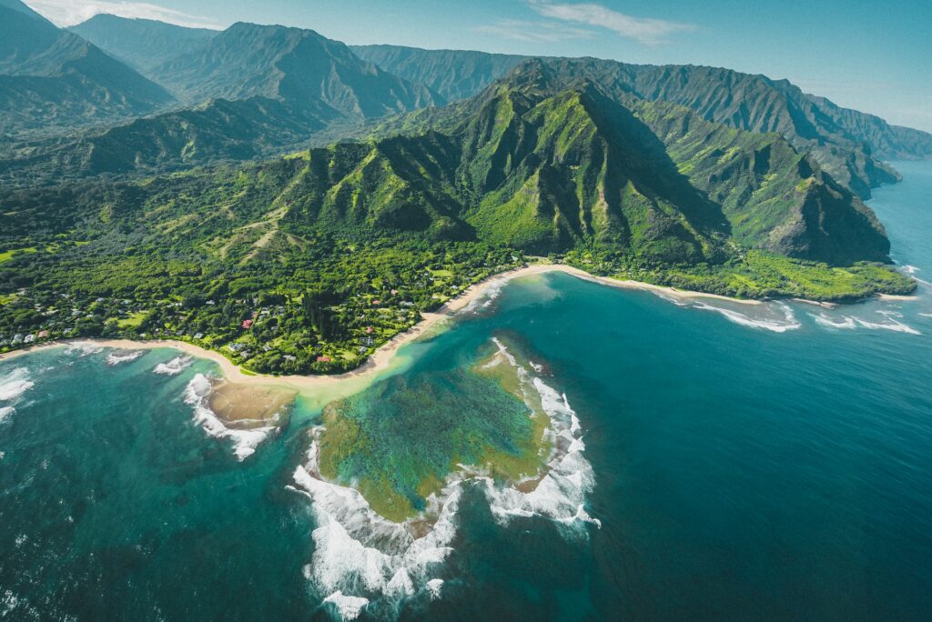 Vista aérea de montanhas com vegetação vasta no topo e uma parte do mar cercando as montanhas com águas azuis cristalinas para representar o chip internacional para o Havaí. 