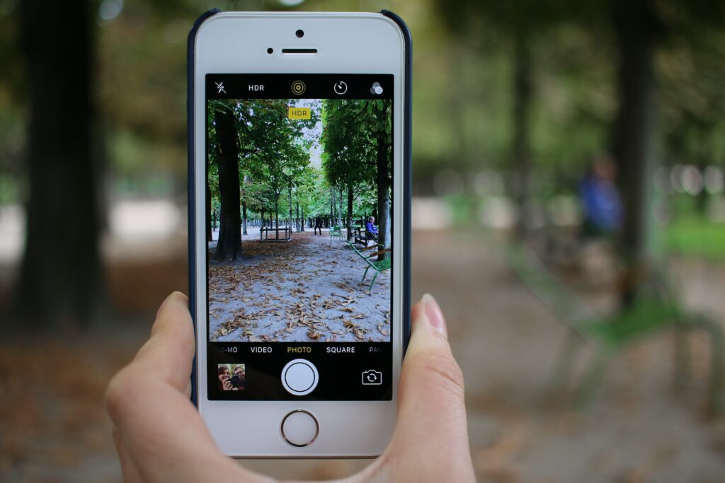 Um celular na vertical fotografando um parque com muitas árvores e bancos verdes em Paris, na França