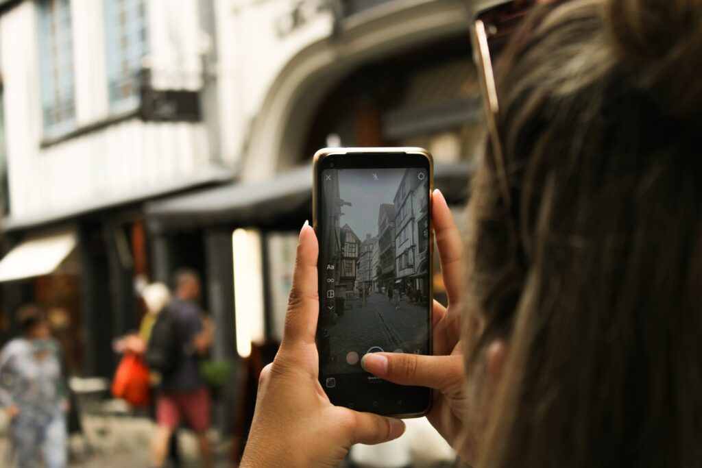 Uma mulher segurando um celular na vertical enquanto fotografa uma rua cheia de prédios antigos em Rouen na França