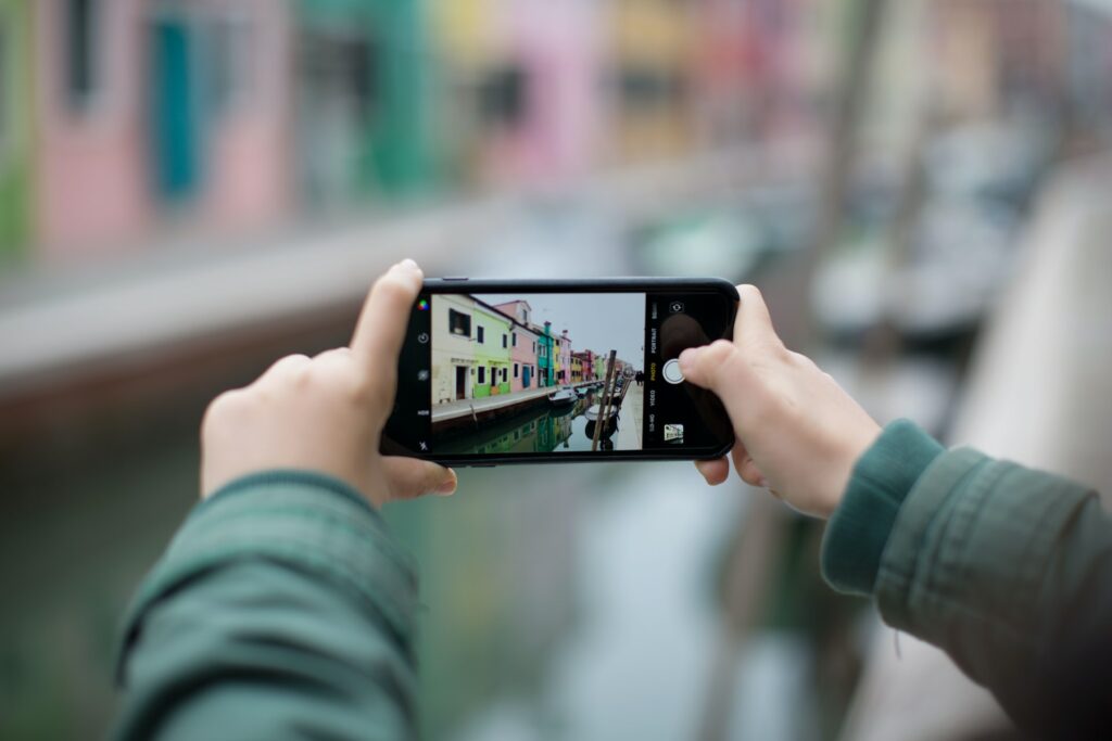 Duas mãos femininas segurando um celular na horizontal enquanto tira uma foto de um canal de Veneza na Itália