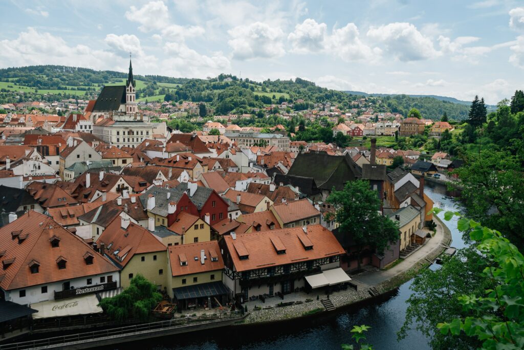 Vista de cima da cidade de Český Krumlov, República Tcheca, durante o dia com um rio em volta a cidade com várias casas. Representa seguro viagem para o Leste Europeu.