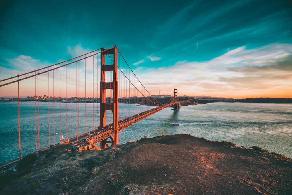 Ponte Golden Gate de San Francisco para ilustrar o post sobre chip internacional para a Califórnia. A ponto é vermelha e vários carros passam por ela. O céu é azul acima e o mar está embaixo. Ao longe está a cidade. - Foto: Joseph Barrientos via Unsplash
