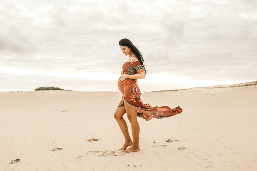 mulher grávida com vestido esvoaçante em meio a dunas para ilustrar o post de seguro viagem para gestante