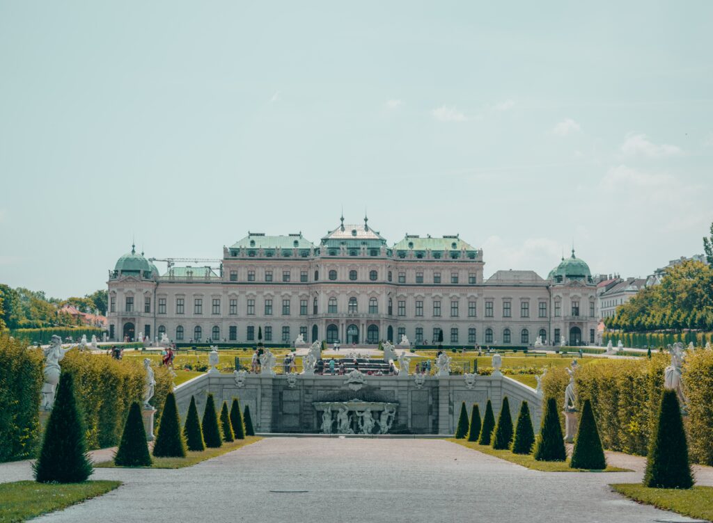 Vista da frente do Palácio Belvedere, Viena durante o dia com um jardim lindo a frente e ao fundo o palácio.