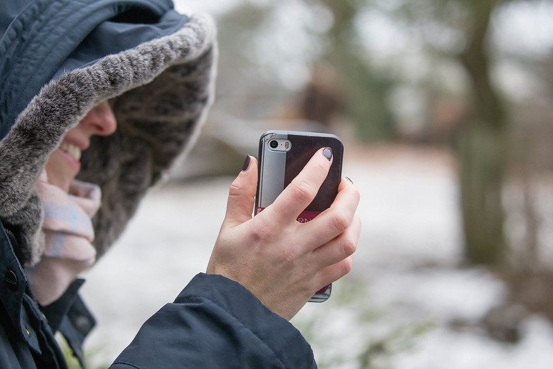 Pessoa de perfil agasalhada, segurando celular da marca Apple na neve em Estocolmo, Suécia.