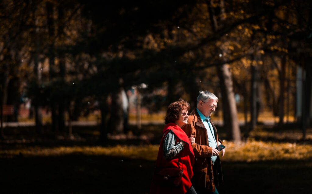 Um casal de idosos andando dentro de um parque de braços dados