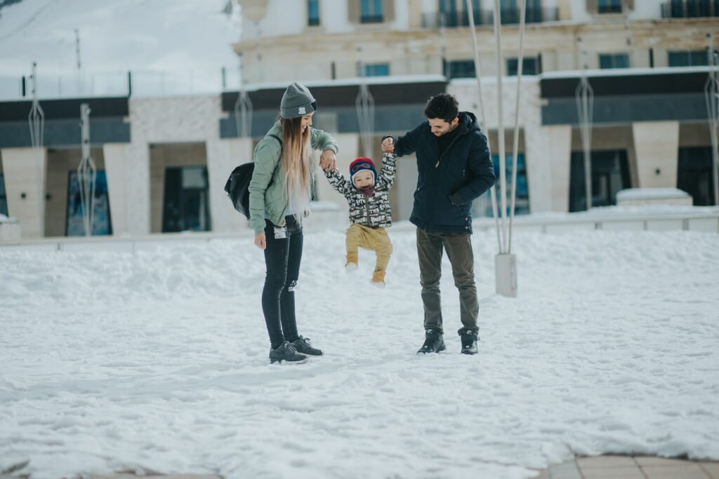 Uma mulher e um homem na neve segurando um menino pequeno pelos braços para ele pular pela neve