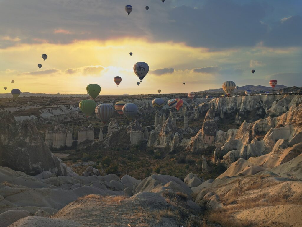 Vários balões de ar coloridos sobrevoando área rochosa na Capadócia. Ao fundo está de dia, no final da tarde. Foto usada para ilustrar post de chip internacional para a Capadócia.