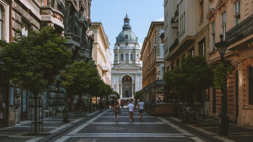 Pessoas andando na calçada em direção a Basílica de Santo Estêvão na Hungria durante o dia.