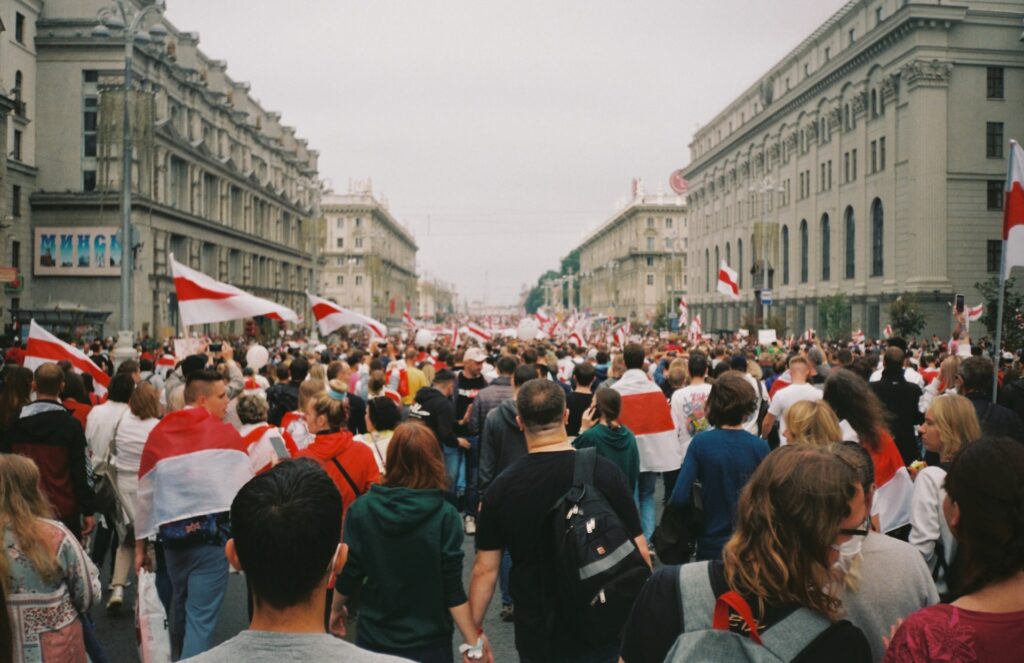 Foto de pessoas andando na rua durante o dia com várias bandeiras branca e vermelha. 