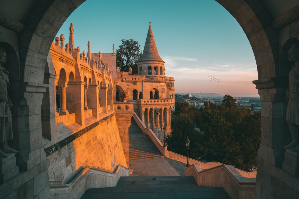 Imagem de um mirante em Budapeste chamado Fisherman's Bastion com uma arquitetura parecendo castelo e algumas escadas durante o pôr do sol.