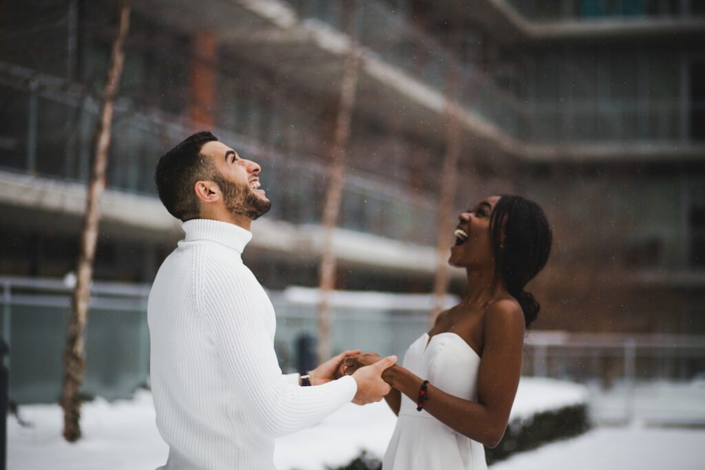 casal no Canadá com neve ao fundo dando as mãos vestidos de branco bem felizes