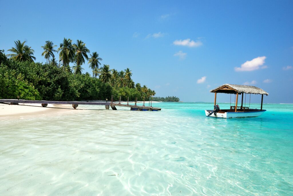Vista do mar azul claro no Medhufushi Island Resort, Maldivas, durante o dia com barco no mar. - Representa chip internacional para Maldivas.