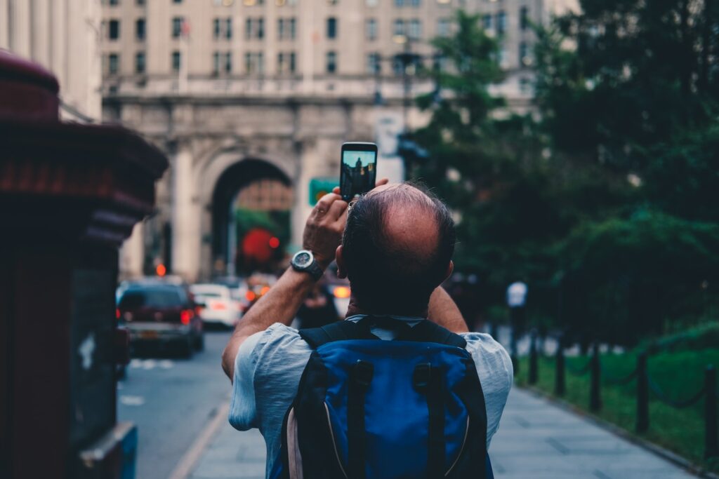 Homem de mochila azul nas costas, de costas, tirando foto de um monumento histórico em Nova York
