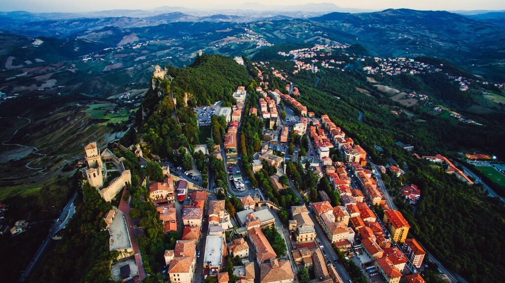 Vista de cima de San Marino, imagem colorida, cheia de casas, estradas e árvores.