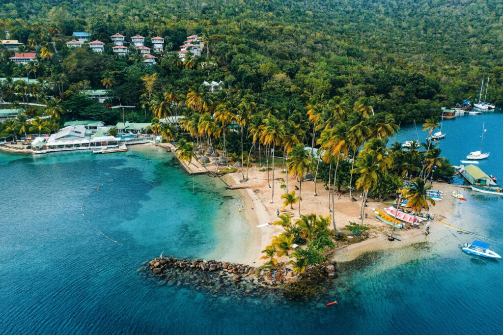 Vista de cima da Marigot Bay em Santa Lúcia durante o dia com mar em tom azul e areia branca com coqueiros. Representa chip internacional para o Caribe.