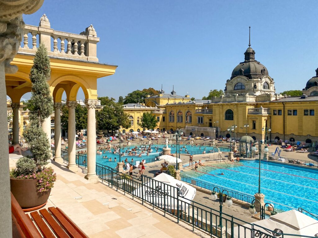 Prédio em amarelo ao lado de piscinas com pessoas dentro durante o dia, ilustrando post chip internacional para Budapeste.