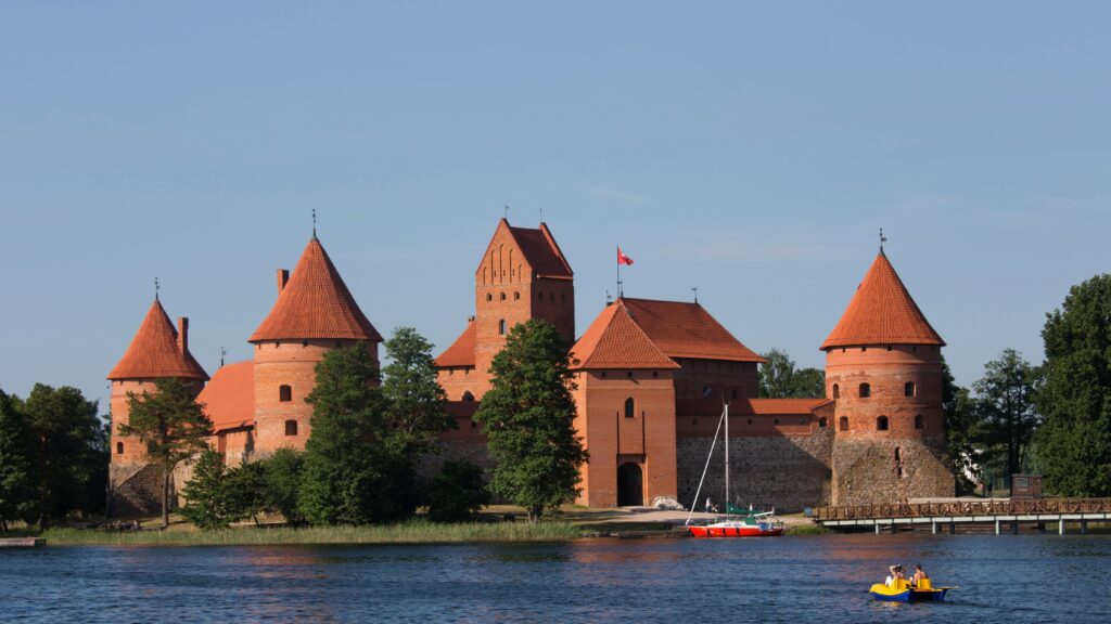 Vista da frente do Castelo da Ilha de Trakai durante o dia com um rio a frente e ao fundo o castelo. Representa chip internacional para a Lituânia.