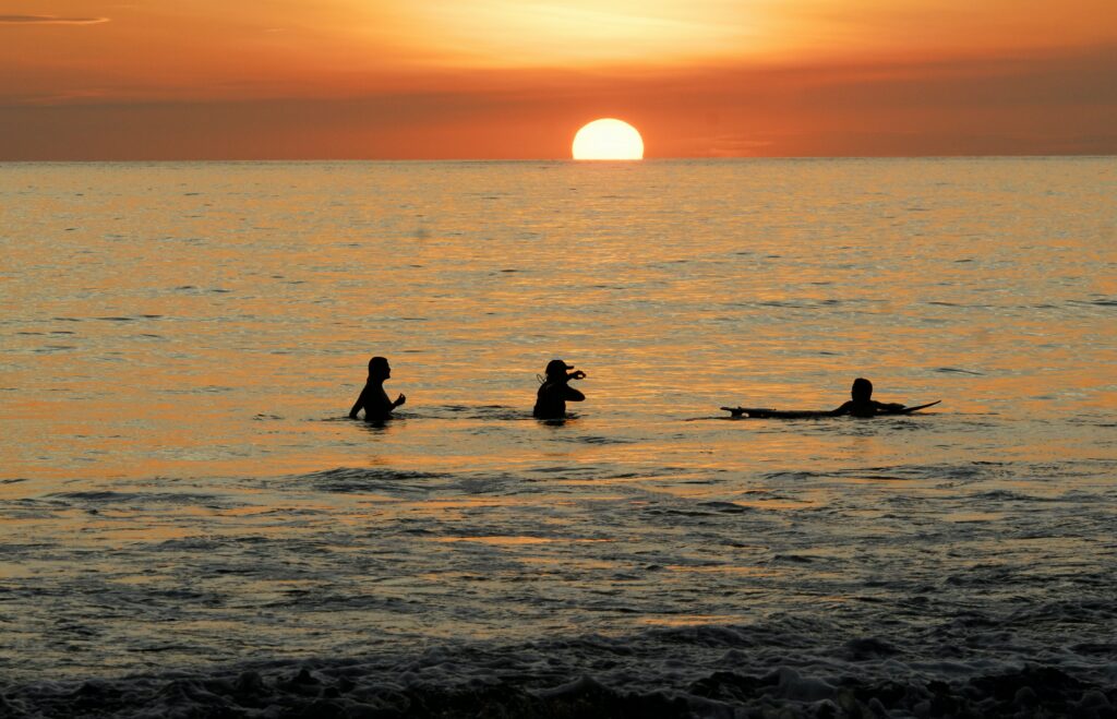 Três silhuetas de pessoas nadando na praia da Província de Puntarenas, Quentos, Costa Rica. O sol está se pondo no horizonte. Foto para ilustrar os benefícios do chip internacional para a América Central.