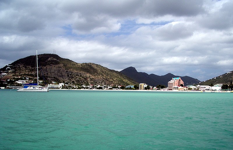 A foto nos mostra o mar em St Maarten, há um navio passando. Em terra firme, vemos prédios e casas. Ao fundo, algumas montanhas. Foto para ilustrar o post sobre chip internacional para St Maarten.