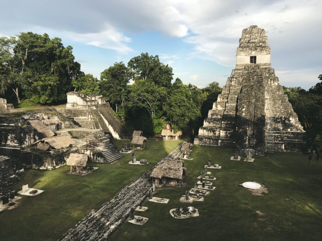 A foto mostra ruínas do templo maia chamado Tikal, em Guatemala. Está de dia, em sua volta há várias árvores e uma grama bem esverdeada. Foto utilizada para representar o post de chip internacional para Guatemala.